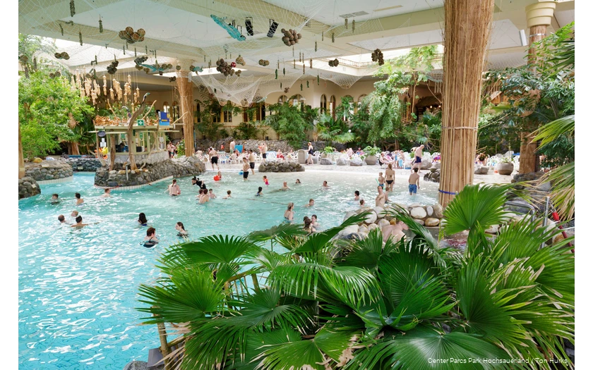 Some people swim in the Aqua Mundo adventure pool, which is decorated with numerous palm trees, making it look like a beach.