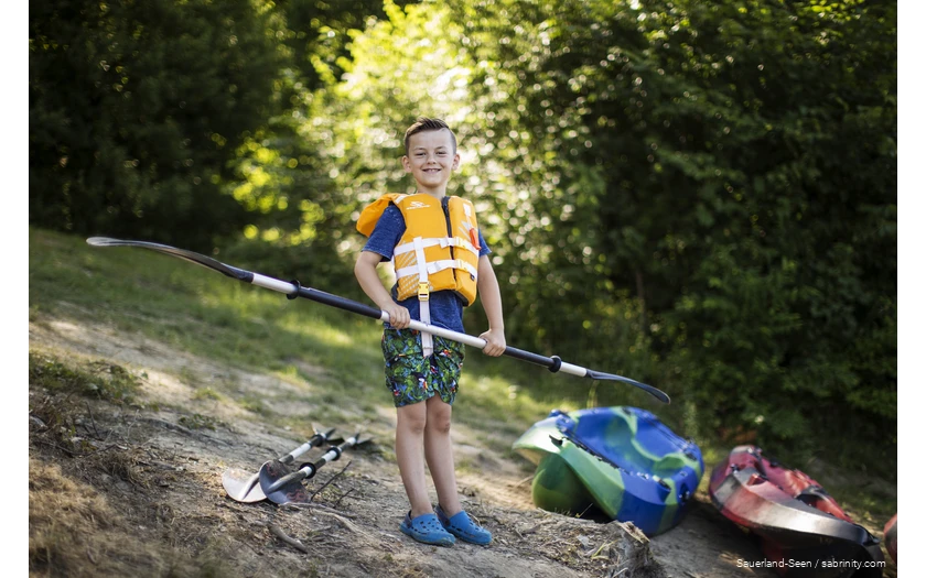 Boy with life jacket looking forward to canoeing with a paddle in his hand.