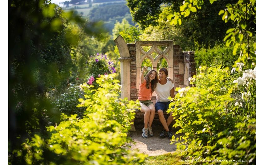 Mother and daughter sit in a blooming garden and take a selfie.