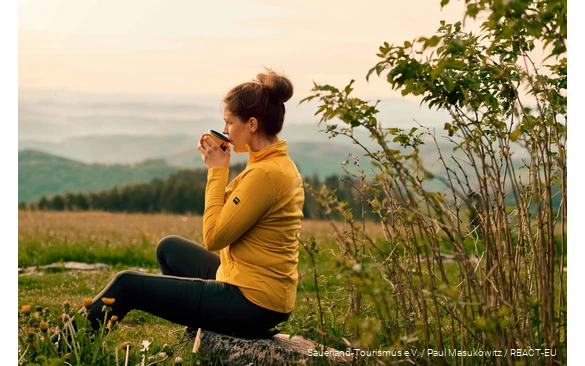 Een wandelaar geniet van haar pauze met een kopje koffie en uitzicht over het landschap.