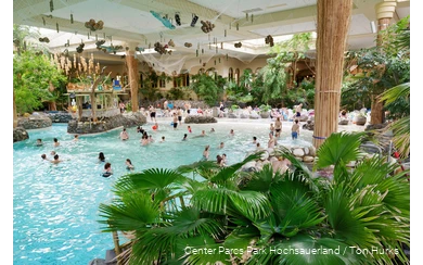 Einige Menschen baden im Erlebnisbad Aqua Mundo, das mit zahlreichen Palmen dekoriert ist, wodurch es wie ein Strand aussieht.