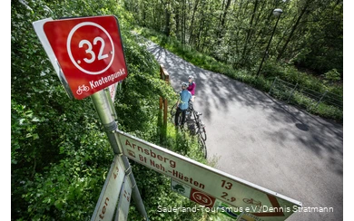 Bord met een kruispuntbevestiging. Twee fietsers op de achtergrond