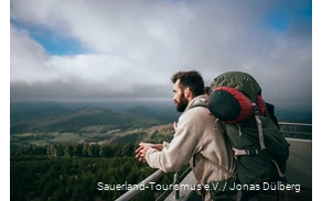 Ein Wanderer mit Mehrtagesrucksack genießt den Blick vom Bollerbergturm.