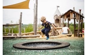 Junge springt auf einem Trampolin, im Hintergrund ein Spielplatz