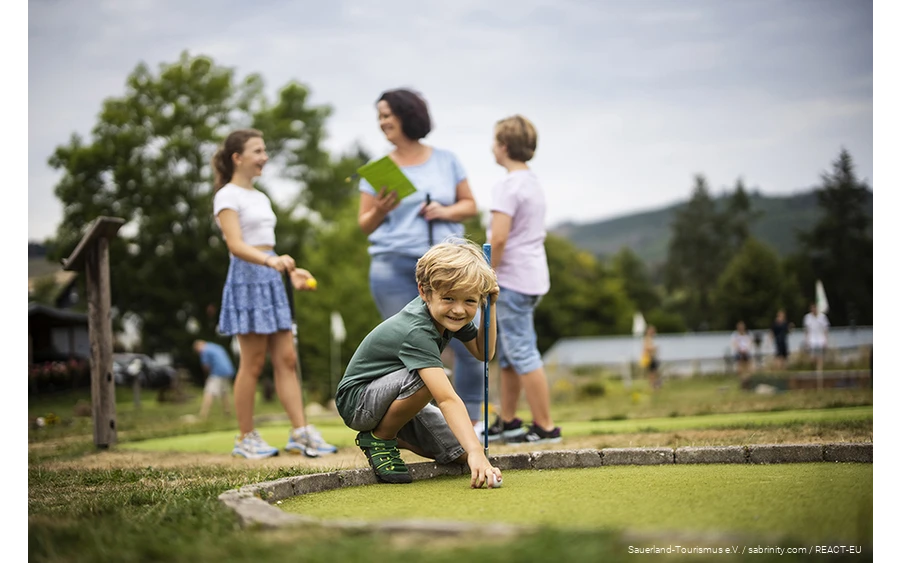A family playing mini golf at Diemelsee. A son prepares his next shot.