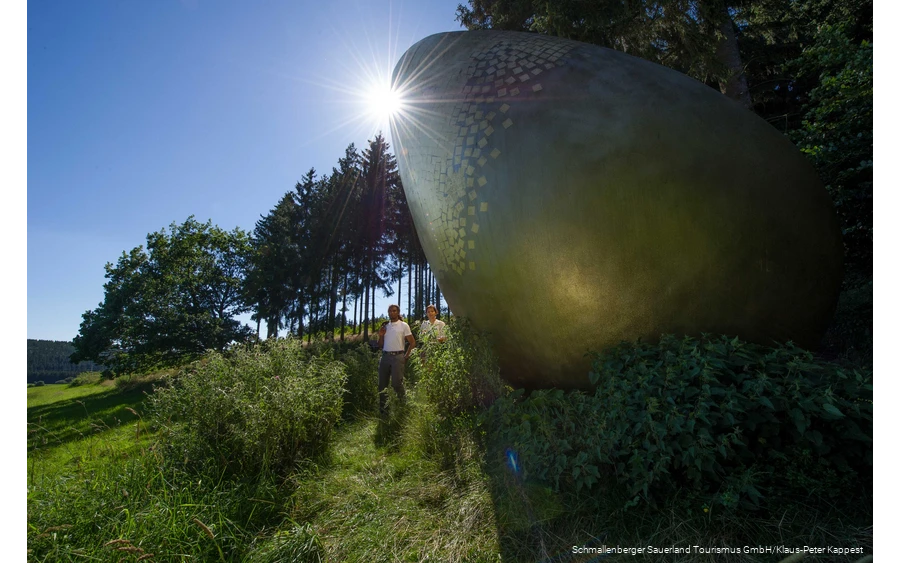 Zwei Wanderer am "goldenen Ei" auf dem WaldSkulpturen-Weg.