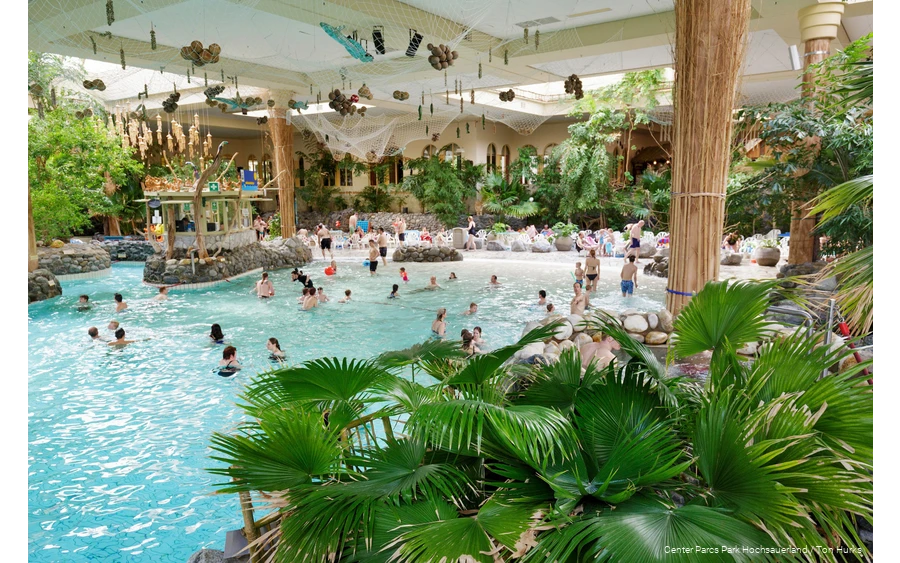 Some people swim in the Aqua Mundo adventure pool, which is decorated with numerous palm trees, making it look like a beach.
