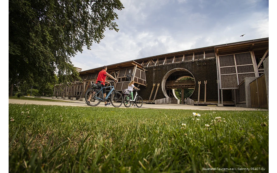 Two cyclists pushing bicycles in front of the Gradierwerk in Bad Sassendorf