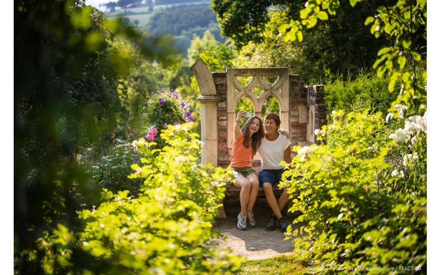 Mother and daughter sit in a blooming garden and take a selfie.