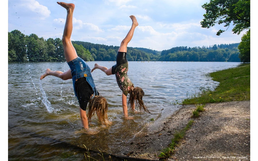 Two girls doing a handstand on the bank of a dam.