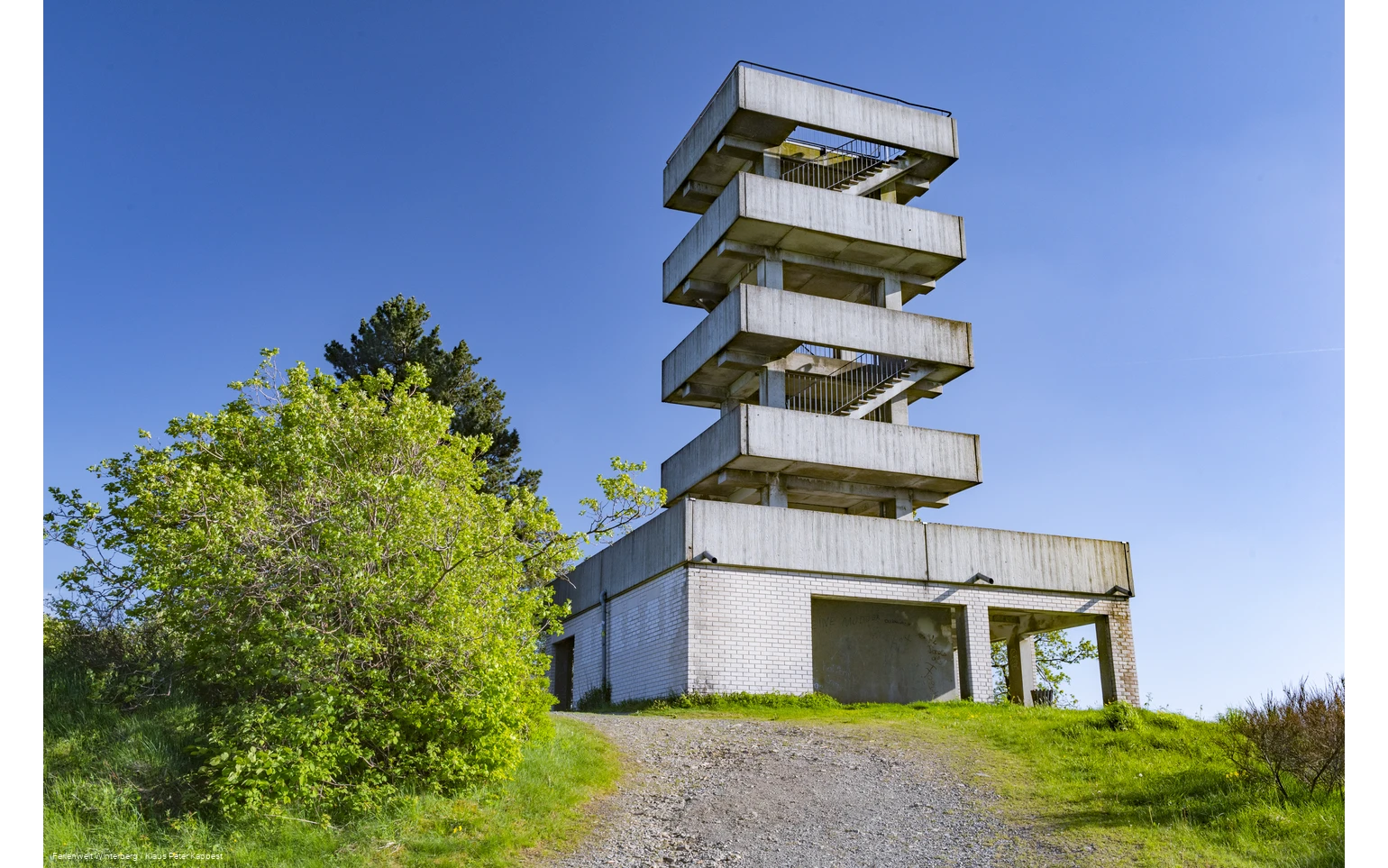 Turm aus Beton mit mehreren Etagen und Treppenaufgängen vor blauem Himmel.