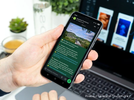 Ein Smartphone wird in der Hand gehalten. Auf dem Bildschirm sieht man einen Post im neuen WhatsApp-Kanal des Sauerland-Tourismus.