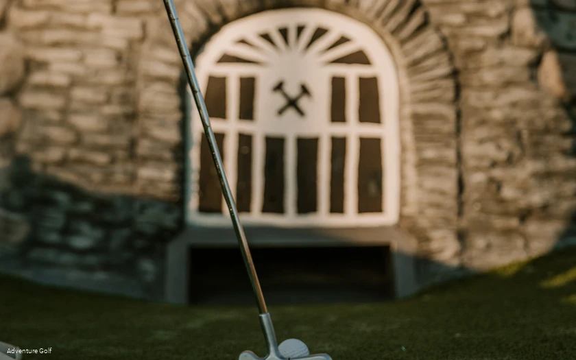 Ein Golfball wird in Richtung eines nachgebauten Bergwerk-Eingangs geschlagen.