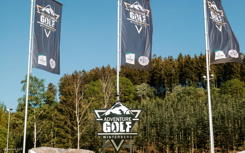 Drei Fahnen mit der Aufschrift Adventure Golf und einem Schild mit der selben Aufschrift.