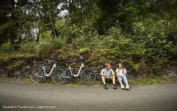 A couple of cyclists take a break at the side of the road.