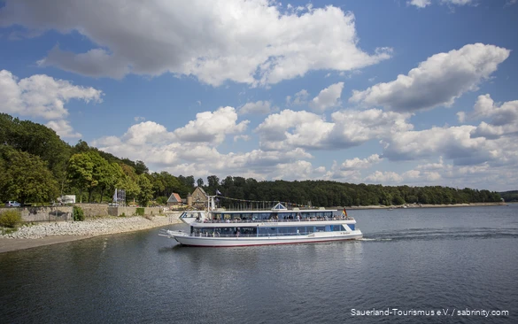 Der Möhnesee an einem Sommertag mit einem Personenschiff voller Menschen im Zentrum