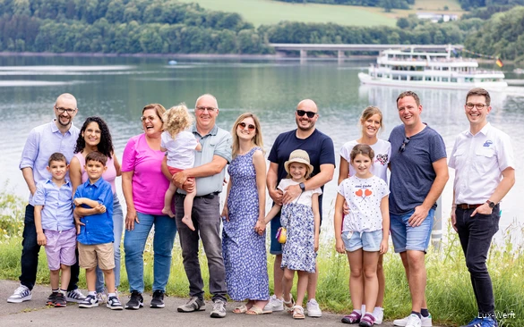 Een lachende groep staat aan de oever van het Biggesee met een schip op de achtergrond