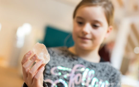 Fokus liegt auf Salzkristall in der Hand von einem Mädchen, das eher verschwommen ist.
