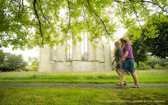 Zwei Frauen in sommerlicher Kleidung laufen an der Stiftsruine in Lippstadt vorbei und lachen miteinander.