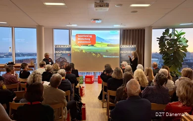 A large group of people are watching a presentation. Next to them are two women who are giving a presentation.