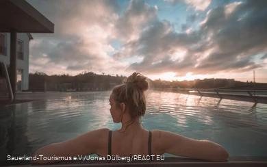 A woman photographed from behind enjoying the pool at sunrise