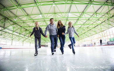 Father, mother and two daughters skate hand-in-hand.