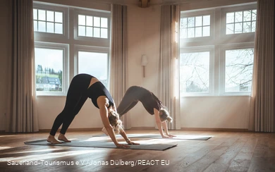 Twee vrouwen doen een yoga-oefening in een lichtovergoten kamer