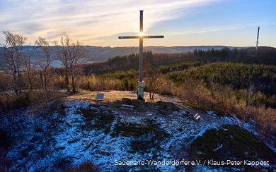 Landscape shot of the summit cross on the Olsberg at sunrise. There is a thin layer of snow.