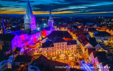 Vogelperspektive auf den Soester Weihnachtsmarkt mit beleuchteten Hütten und bunt angestrahlten Kirchen.