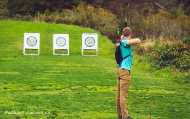 A man doing archery in the meadow.