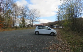 Ein kleines weißes Auto parkt auf einem Parkplatz am Wegesrand.