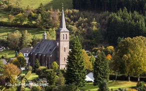 Drohnenaufnahmeeiner Kirche umgeben von Wiesen und Wäldern.