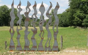 Roestende metalen stèles in de vorm van vuurvlammen op een weiland