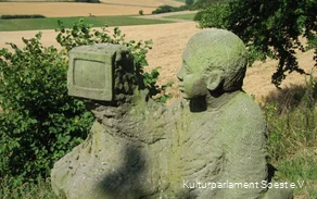 Menschliche Steinskulptur schaut in einen Fernseher umgeben von Fernsicht.