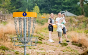 Eine Familie mit zwei Kindern beim Disc-Golf spielen.