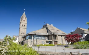 Eine Kirche vor blauem Himmel mit Bäumen und Sträuchern im Vordergrund.