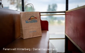 Eine Winterberger Einkaufstüte aus Papier auf einer roten Sitzbank.