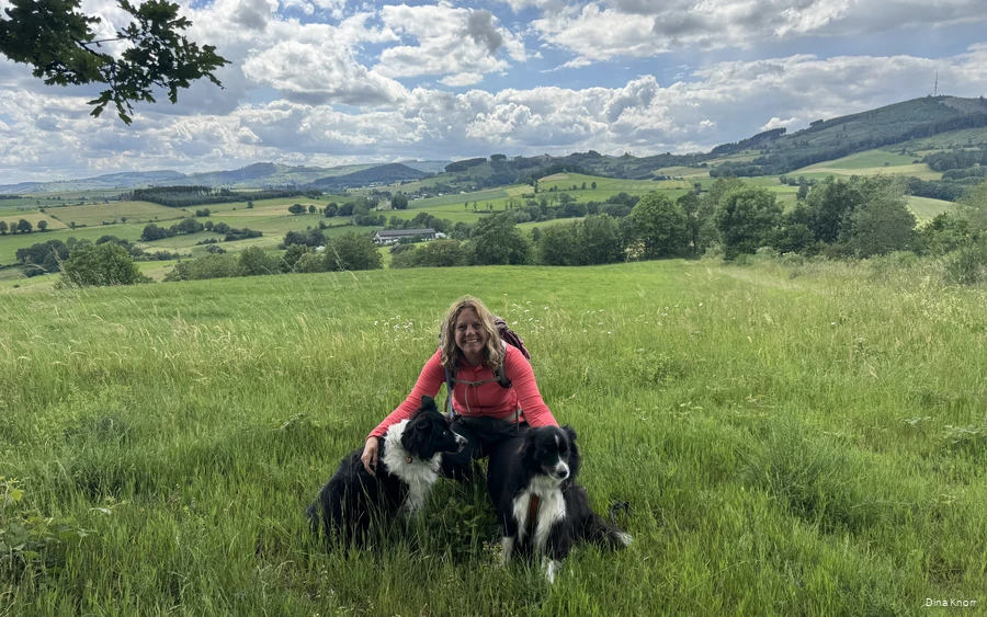 Bloggerin Dina Knorr posiert mit ihren beiden Hunden vor der grünen Sauerländer Landschaft auf einer ihrer Wanderrunden.