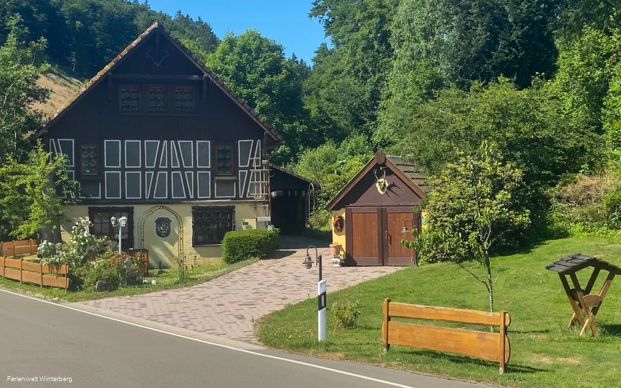 Ein altes Gebäude mit Fachwerk, davor die Einfahrt zum Grundstück und eine kleine Hütte.