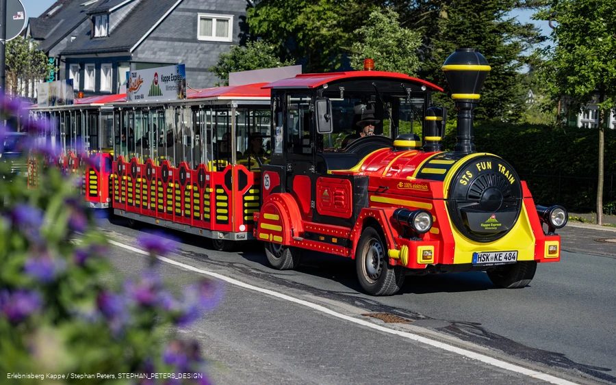 Eine rot-gelbe Eisenbahn fährt die Straße entlang.