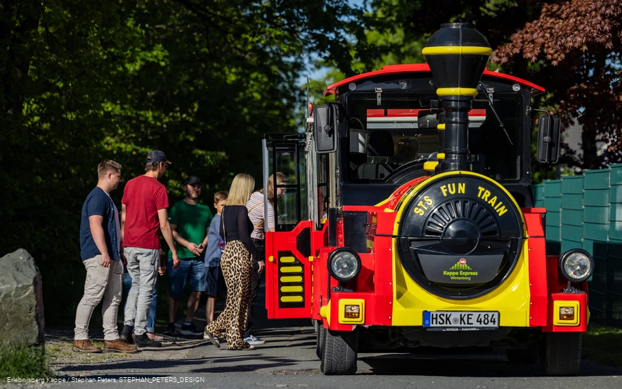 Einige Personen steigen in eine rot-gelbe Eisenbahn ein.