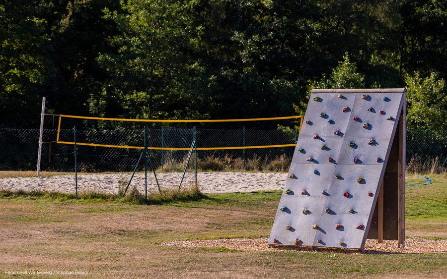 Kletterwand mit Volleybalfeld im Hintergrund.