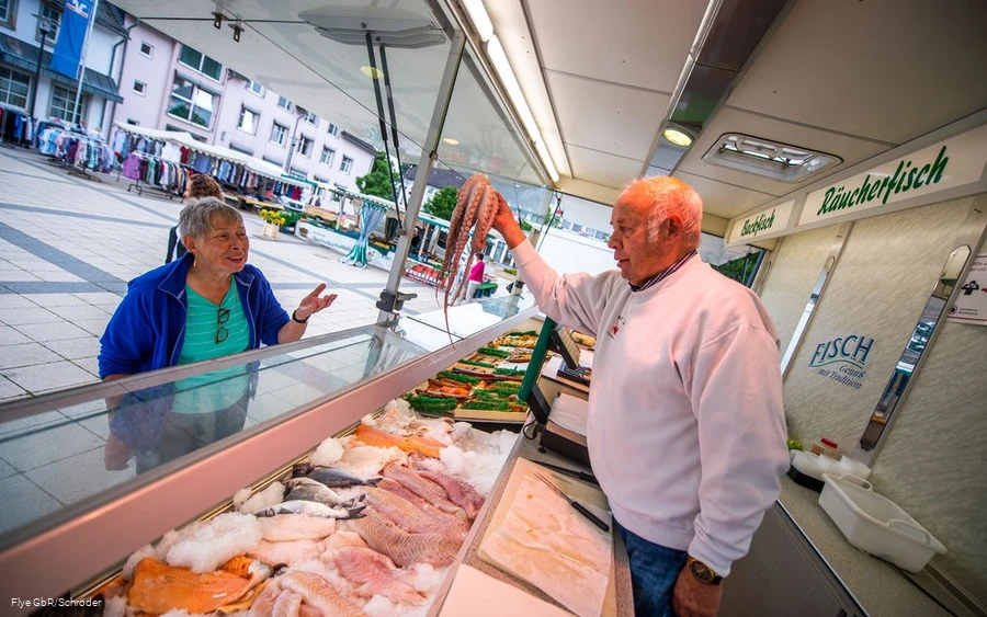 Fischhändler bietet einer Dame Tintenfisch an Fischhändler bietet einer Dame Tintenfisch an