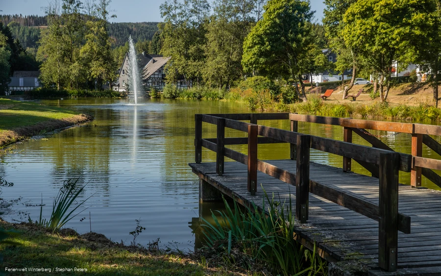 Blick auf einen See mit einer Fontäne in der Mitte und einem Bootssteg im Vordergrund.