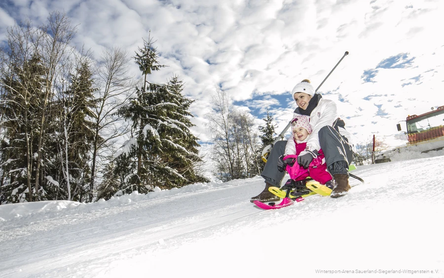 Frau fährt mit ihrem Kind auf dem Schlitten die Piste herunter.