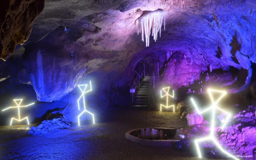 Die Dechenhöhle ist mit bunten Lichtern ausgeleuchtet und beleuchtete Strichmännchen stehen an verschiedenen Ecken.
