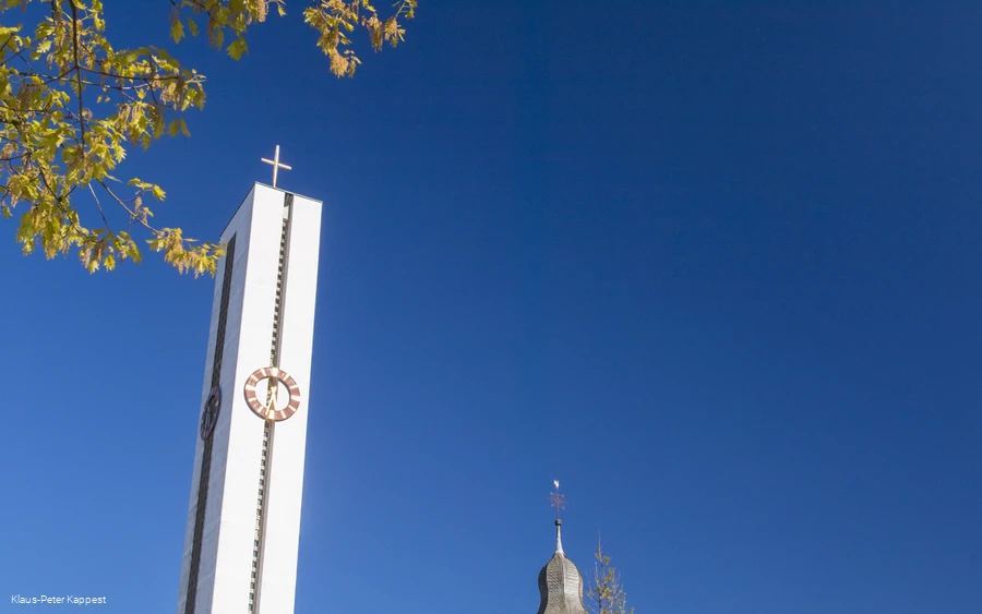 Eine Kirche neben einem hohen Kirchturm mit Turmuhr vor blauem Himmel.