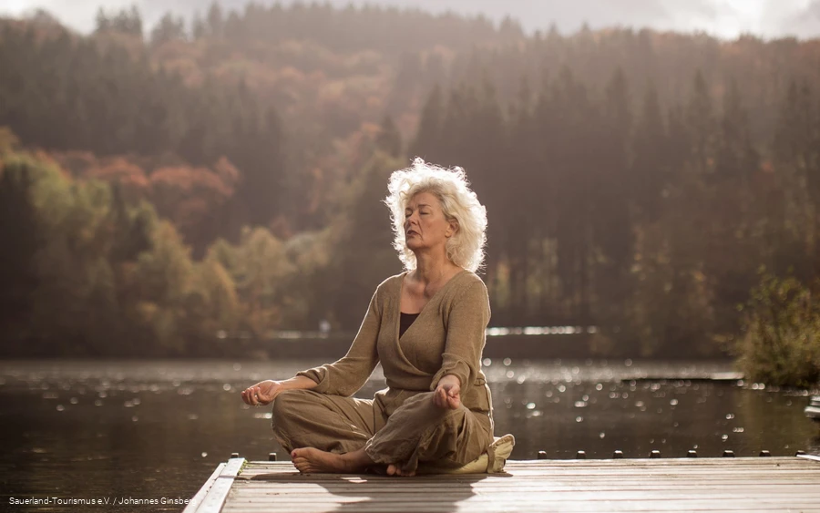 A woman relaxes with yoga exercises by a lake.