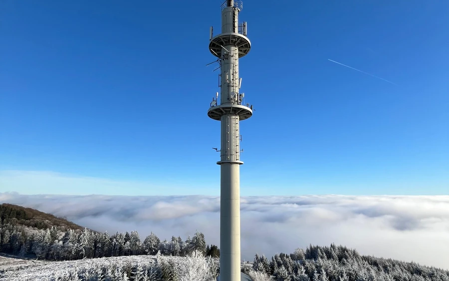 Fernmeldeturm umgeben von Schnee und Nebel vor blauem Himmel.