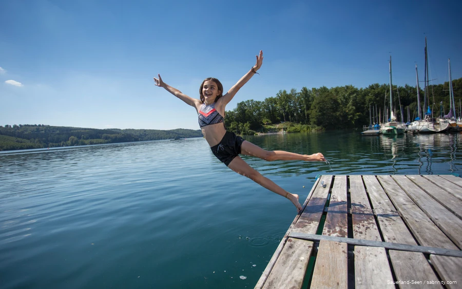 Ein Mädchen springt vom Steg in den See.